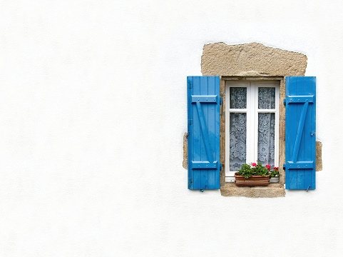 Blue shuttered window on white stucco wall with geraniums in window box
