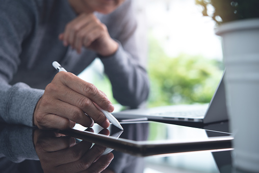 Asian casual business man, website designer with stylus pen touching on digital tablet, working on laptop computer, connecting internet network on table in office, close up. E-business, Online working