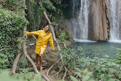 A smiling woman in a yellow coat walks by the waterfall.