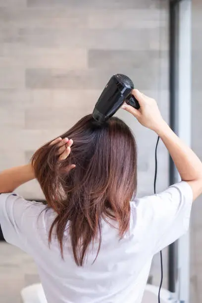 young woman using hair dryer at home or hotel. Hairstyles and lifestyle concepts