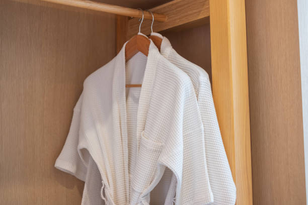 White clean bathrobe hanging in wooden wardrobe at luxury hotel or home. Relax and travel concept White clean bathrobe hanging in wooden wardrobe at luxury hotel or home. Relax and travel concept ceremonial robe stock pictures, royalty-free photos & images
