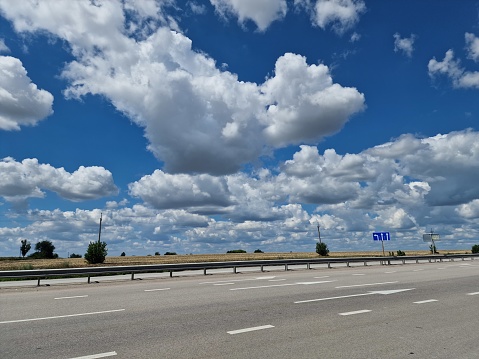 White clouds float across the blue sky over the road