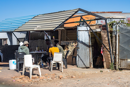 Young men sitting outside Touks Beauty & Hair Salon which performs male hair cuts at Katutura Township near Windhoek in Khomas Region, Namibia