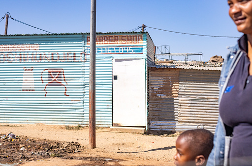 A woman and her child walking past a Barber Shop at Katutura Township near Windhoek in Khomas Region, Namibia