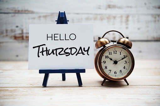 Hello Thursday text with alarm clock on wooden background