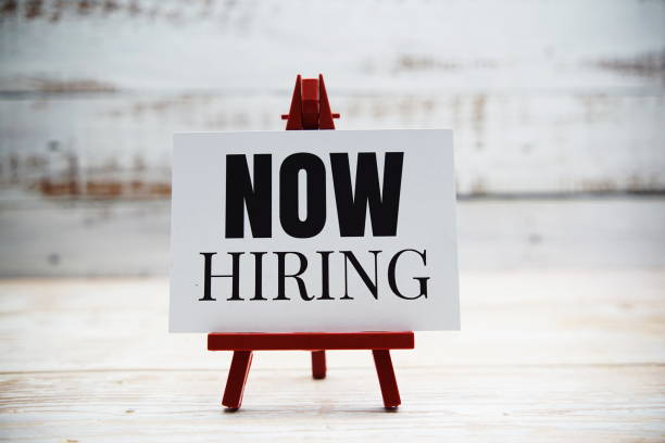 istock Now Hiring text on paper card with wooden background 1410021979