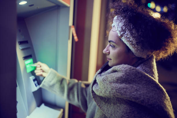 istock Young woman withdrawing money from ATM by night. 1410022111