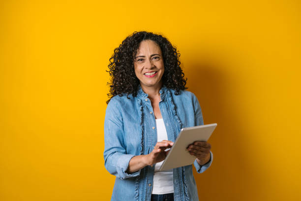 hispanic adult business woman portrait on yellow background in Mexico Latin America hispanic adult business woman portrait on yellow background in Mexico Latin America old woman smiling tablet stock pictures, royalty-free photos & images