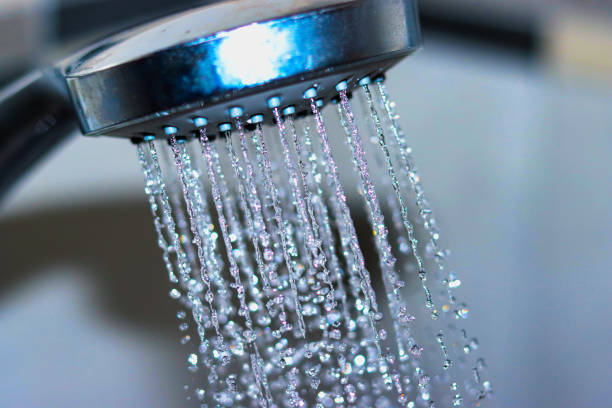 Silver shower head spraying water, low angle, tight focus on droplets, clean image with copy space