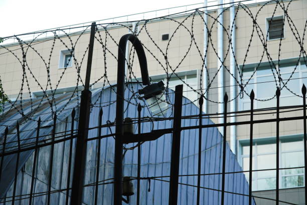 istock Barbed wire on a pole above a metal fence with a lantern against a hight bilding 1410028051