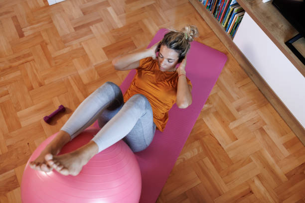 Young woman doing sit-ups on a fitness ball at home stock photo