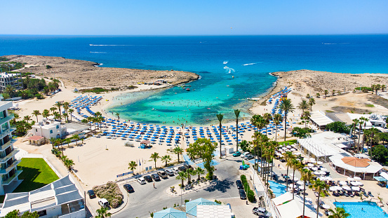Aerial bird's eye view of Vathia Gonia beach, Ayia Napa, Famagusta, Cyprus. The landmark tourist attraction rocky bay at sunrise with golden sand, sunbeds, sea restaurants in Agia Napa on summer holidays, from above.