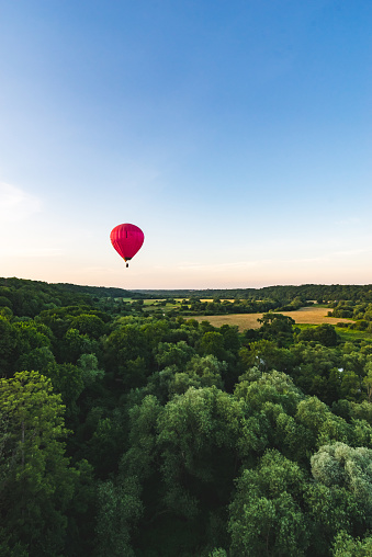 Flying with hot air balloon over forest in the evening, clear blue sky.