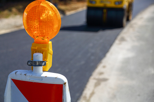 A yellow construction site indicator in front of road works laying new asphalt and steamroller.