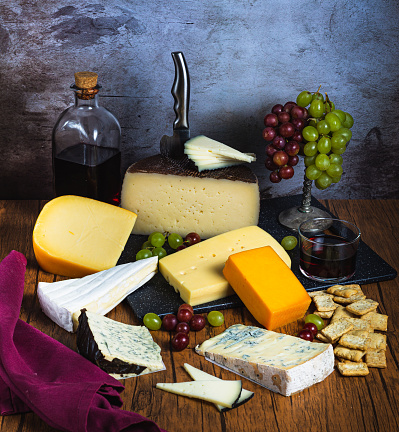 Close-up of a wooden table with various types of cheeses, accompanied by grapes and red wine,