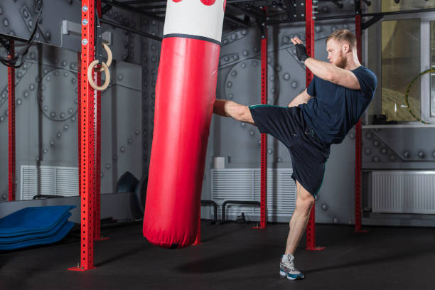 istock Young strong mixed martial arts fighter delivers strong side kick to punching bag. Active exercise in gym. 1410032535