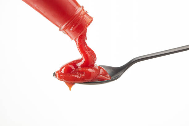 istock Red ketchup flowing from a bottle into a spoon on white background. 1410037339