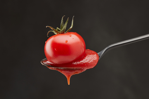 Red tomato and ketchup pouring out of a spoon on a black background. Shallow depth of field
