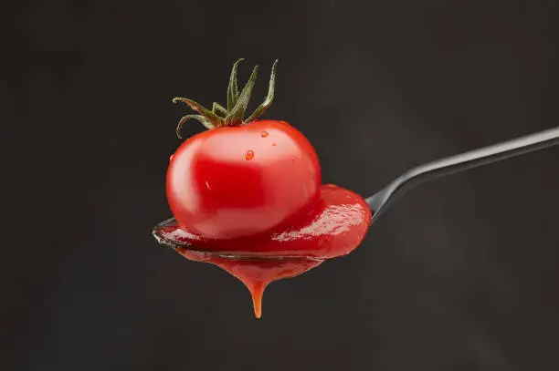 Red tomato and ketchup pouring out of a spoon on a black background. Shallow depth of field