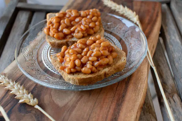 Delicious and healthy plant based protein snack with whole grain toast and baked beans. Served on a plate on wooden background