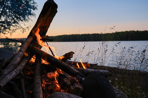 The concept of travel in Russia. White nights in north of Karelia. Light bonfire on shore of Lake Ladoga in evening. The heat from fire.