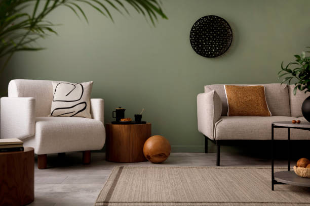istock Creative composition of living room interior with green wall, grey sofa with brown pillow. White armchair with patterned pilow, wooden coffee table with black accessories. Template. 1410040166