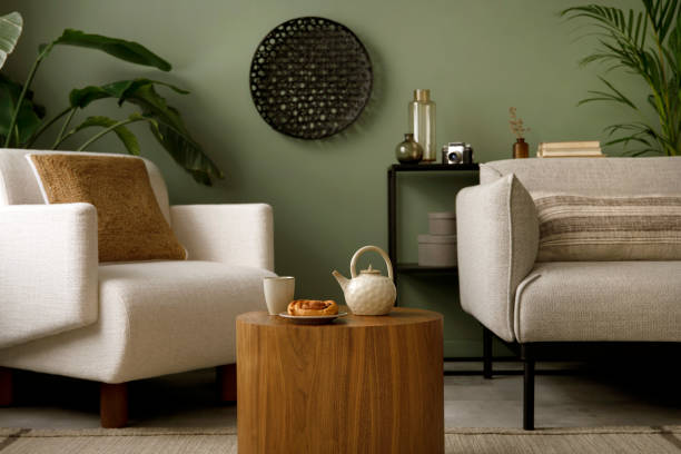 istock Creative composition of living room interior with green wall, grey sofa with grey pillow. White armchair with brown pillow, wooden coffe table with accessories. Black vase with green flower. Template. 1410040285