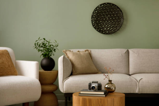 istock Minimalist composition of living room interior with green wall, grey sofa with grey pillow. White armchair with patterned pillow, wooden coffee table with black accessories. Black vase with green flower. Template. 1410040341