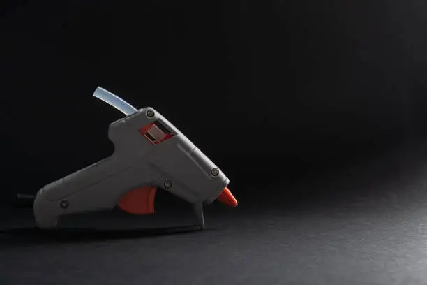 Gray and orange hot glue gun on a dark background