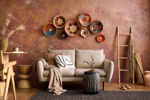 The stylish boho compostion at living room interior with design beige sofa, coffee table, wicker baskets and elegant personal accessories. Brown and white pillows and plaid Cozy apartment. Home decor