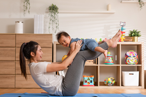 Asian mom playing to adorable infant baby on yoga mat smiling and happiness at home. Mom talking with baby fun and laughing throwing up son in the air exercise together.Relax time.Baby and Mother day