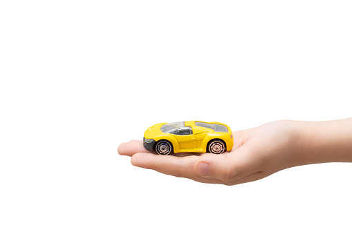 Child hand holding small yellow toy car, isolated on white background.