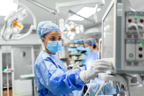 anesthetist working in operating theatre wearing protecive gear checking monitors while sedating patient before surgical procedure in hospital - equipamento médico imagens e fotografias de stock