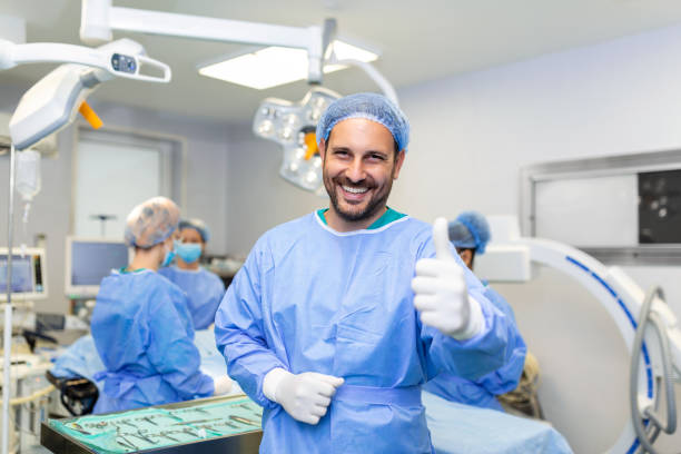 手術室に立って親指を立て、患者に手術する準備ができている若い男性外科医。手術室の男性医療従事者手術服。 - scrubs surgeon standing uniform ストックフォトと画像
