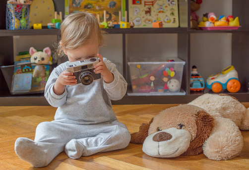 Dulce niño pequeño divirtiéndose en casa jugando con una vieja cámara de fotos, en el suelo. Actividad en interiores para niños photo