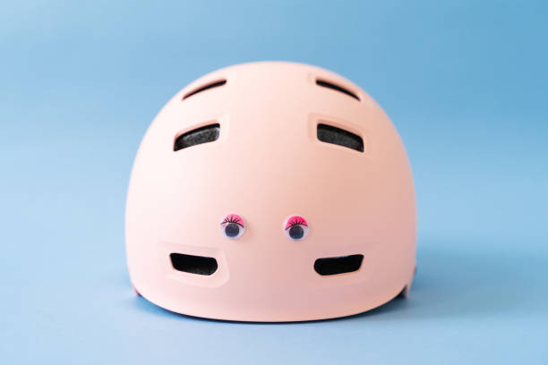 Pink helmet with funny doll eyes on blue background. Childs outdoors activity safety protection stock photo