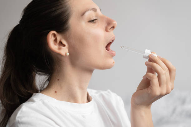 portrait d’une jeune femme aux cheveux foncés prenant un supplément d’huile avec un compte-gouttes en verre. huile de médecine de chanvre cbd appliquée sur la langue - sublingual photos et images de collection