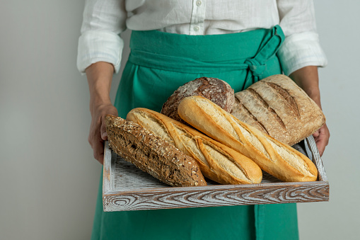Baker female holding fresh baked breads in tray at bakery - stock photo