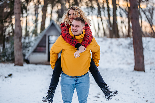 Beautiful young couple piggyback ride in snowy forest.