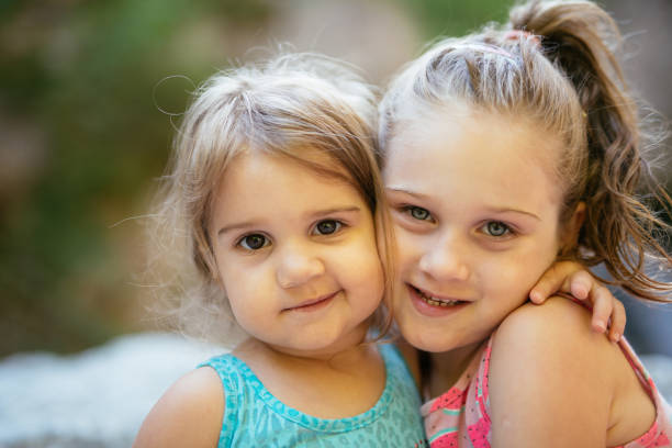 Color image of happy, twin, blonde-haired girls sitting together outside on a summer day.