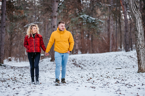 Beautiful young couple walking in snowy forest, holding hands.