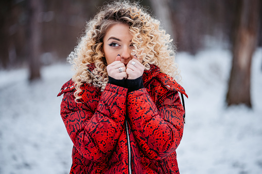 Beautiful young woman feeling cold in a snowy forest. Warming up her hands.