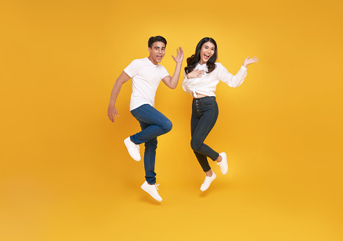 happy excited young asian loving couple jumping isolated over yellow wall background.