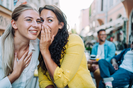 Shot of young happy women talking and laughing while drinking coffee together in a sidewalk cafe.