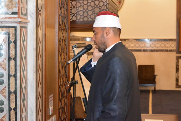 a mosque imam preacher muezzin in front of the microphone reciting adhan azan or calling loudly for the prayer or salah summoning muslims to enter the mosque - adhan imagens e fotografias de stock