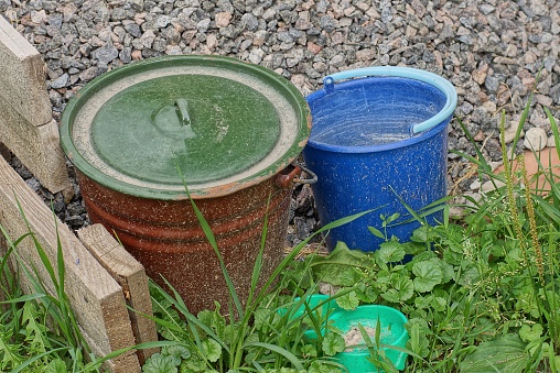 two old metal and plastic buckets stand in the green grass on the street