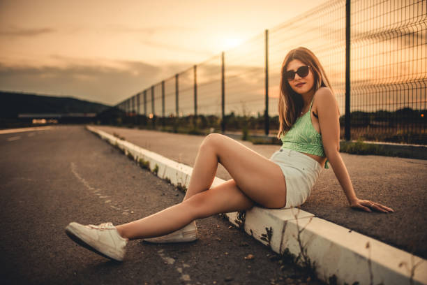Profile of a beautiful young woman sitting on the sidewalk at dawn.