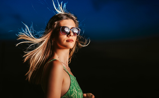 Profile of a beautiful young woman wearing sunglasses and wind blowing out her hair.