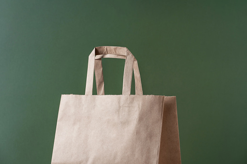 Kraft paper recycled shopping bag on green background minimal concept. Sustainable packaging concept