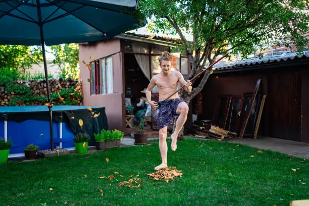 Caucasian ethnicity young adult man gardener playing rock'n'roll during raking old leaves.